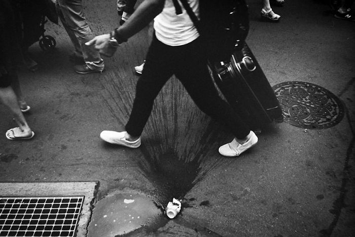 Black and white Japan street photography shot showing pedestrians walking over wet pavement with urban details and suitcase.