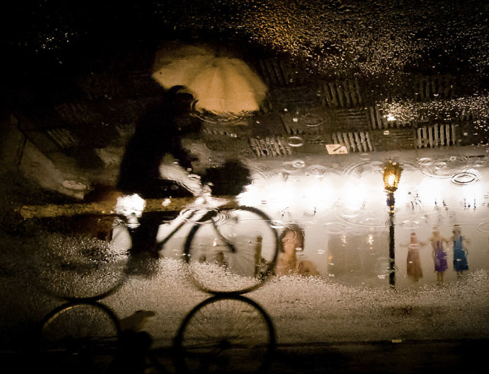 Reflection of a person riding a bicycle with an umbrella in Japan street photography capturing rainy urban scenes.