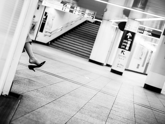Legs of a woman in high heels peeking from a wall in a quiet underground station, Japan street photography style.