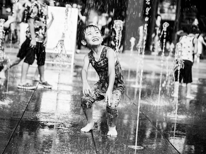 Child playing in water fountain on a busy street in Japan, captured in candid Japan street photography style.
