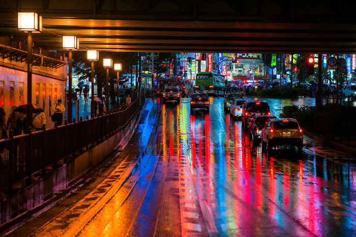 Night street scene in Japan with colorful reflections on wet pavement and cars in a vibrant street photography shot