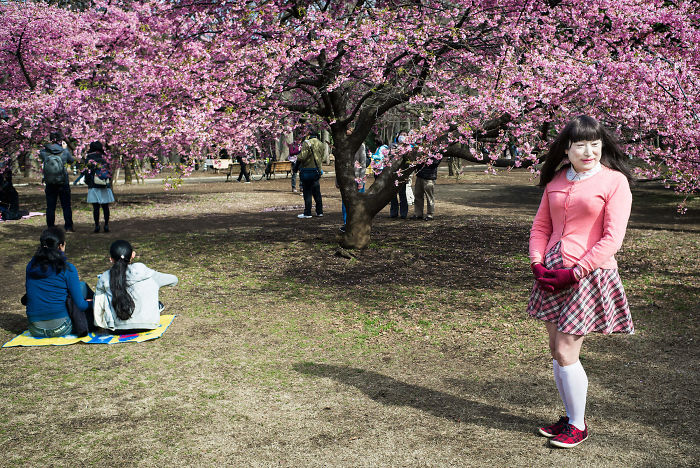 Woman posing under blooming cherry blossoms in a park, part of Japan street photography capturing unique moments and scenes.
