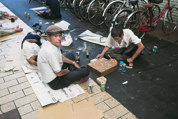 Men playing shogi on a street in Japan surrounded by bicycles and scattered cans, showcasing Japan street photography.