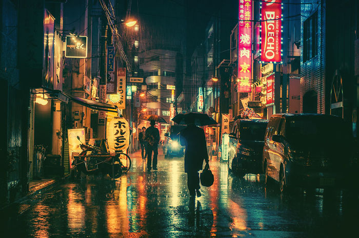 Nighttime Japan street photography scene with rain, neon signs, and a person walking with an umbrella in a vibrant urban setting.