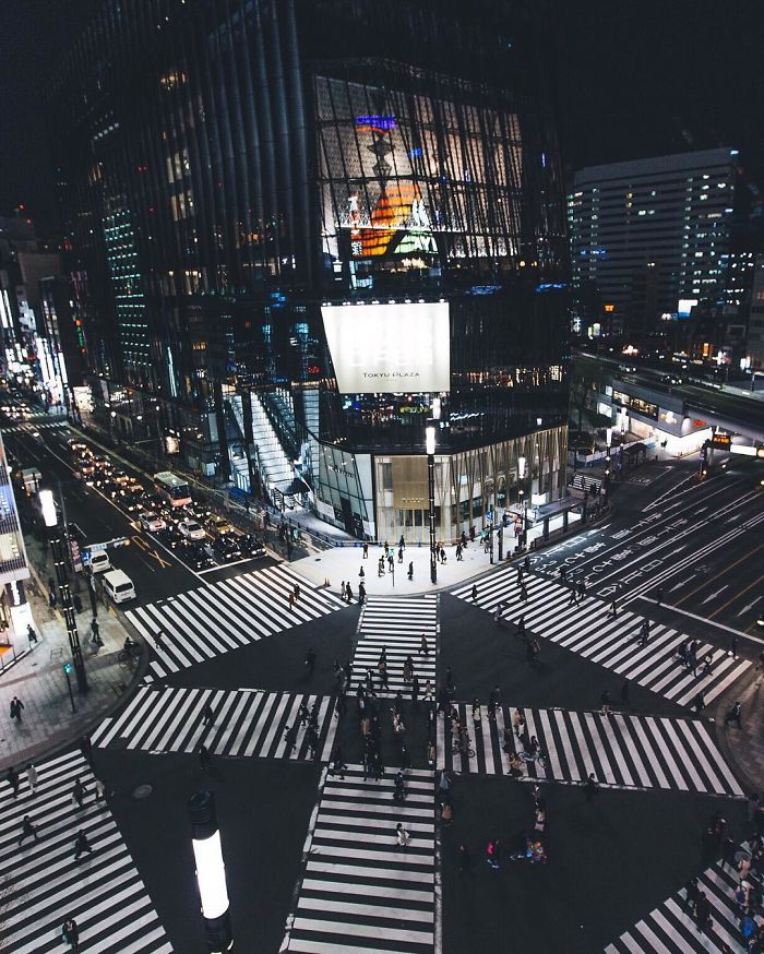 Night view of a busy Tokyo intersection with pedestrians and traffic in Japan street photography style.