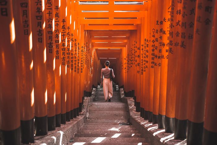 Person walking through vibrant orange torii gates in Japan, showcasing unique Japan street photography scenes.