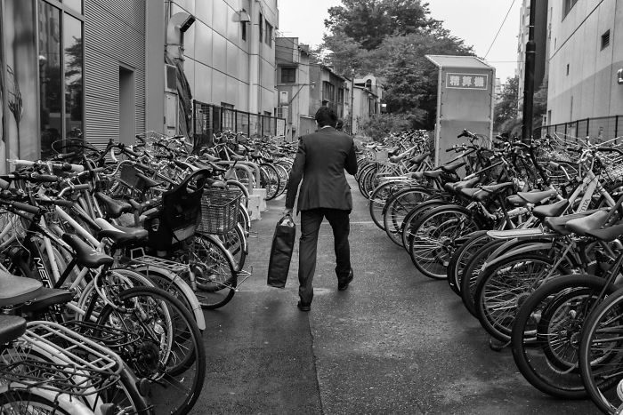 Man in suit walking between rows of bicycles in a narrow alley, a classic example of Japan street photography shots.