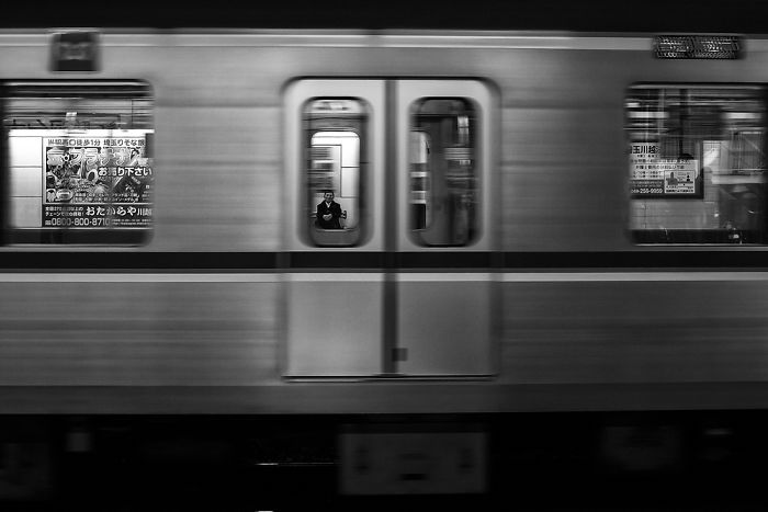 Black and white Japan street photography of a man inside a moving subway train captured in motion blur.