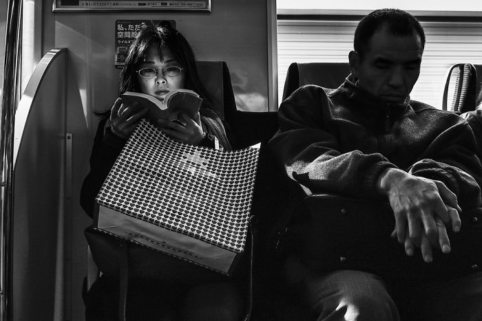 Woman reading a book on a train in Japan, captured in a black and white Japan street photography shot.