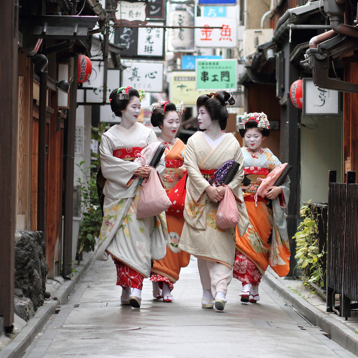 Four geisha women in traditional attire walking down a narrow street, capturing authentic Japan street photography moments.