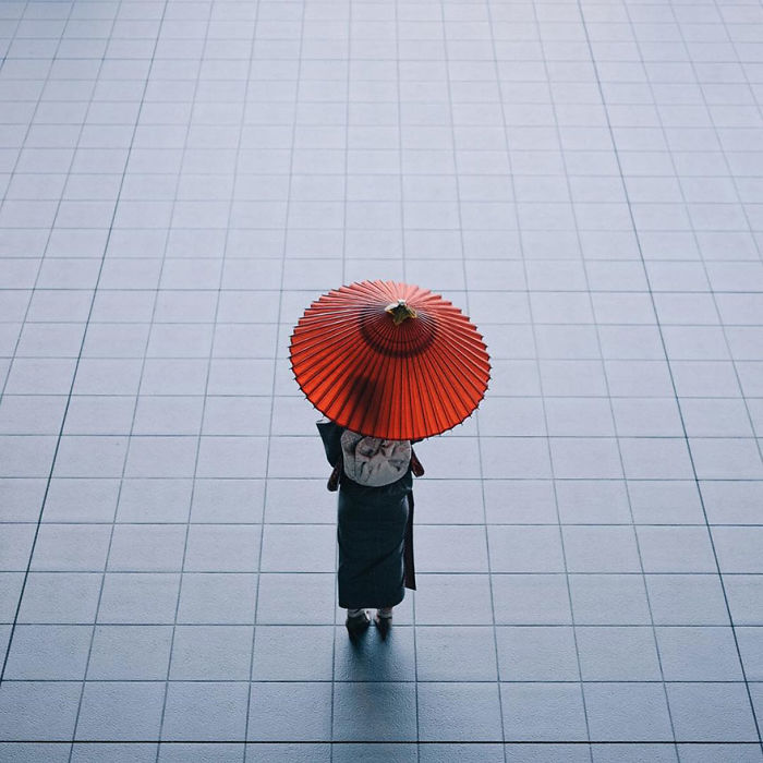 Person in traditional Japanese attire holding a red umbrella, captured in Japan street photography with minimalist tiled background.