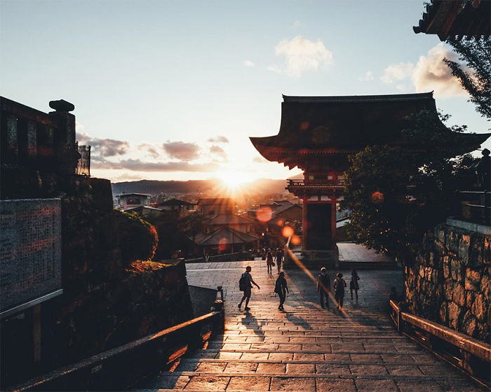 Sunset street photography in Japan showing people walking near traditional temple architecture and stone pathways.