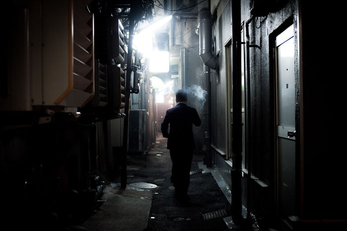 Man smoking in a narrow dark alleyway, Japan street photography capturing the rarely seen urban night scenes of the city.