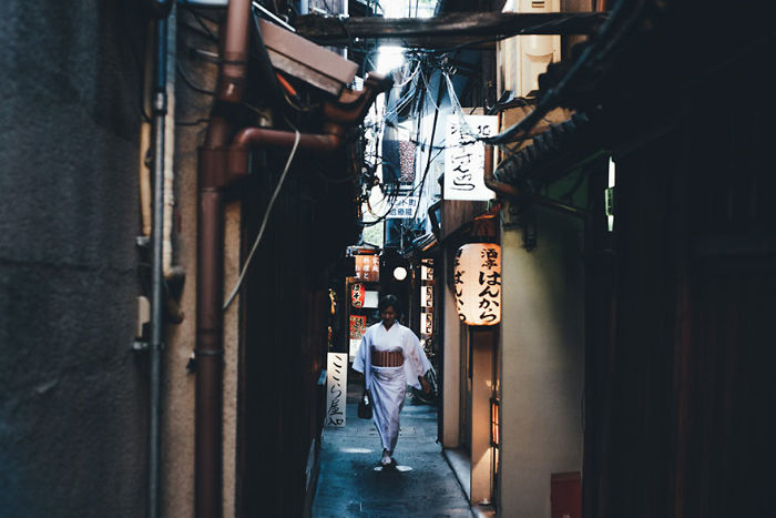 Woman in traditional kimono walking through a narrow alleyway in Japan street photography capturing city life at night.