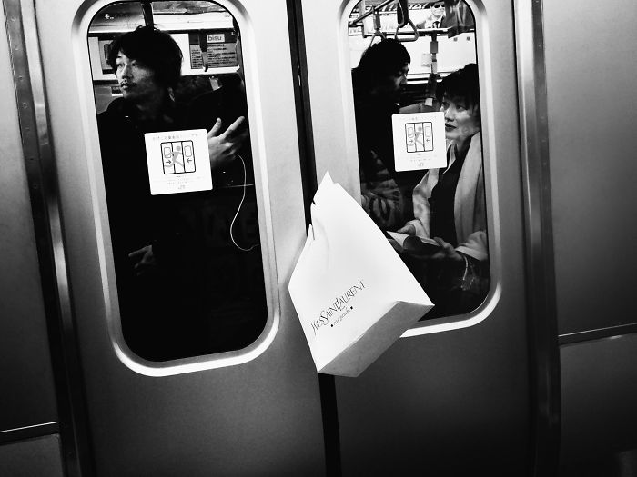 Black and white Japan street photography shot of passengers inside a train with a shopping bag caught in closing doors.