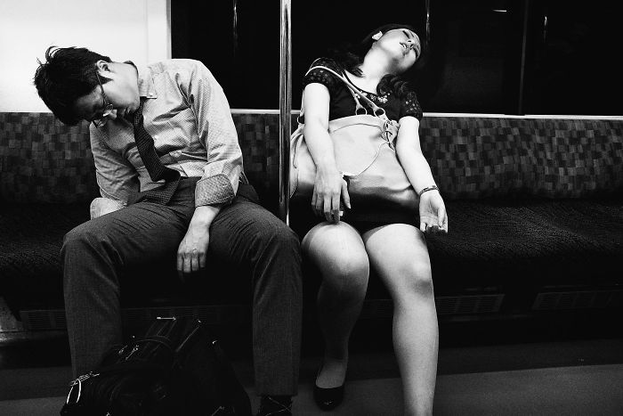Black and white Japan street photography showing two tired passengers sleeping on a train bench, capturing a rare moment.