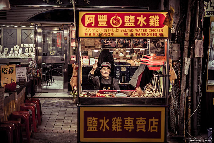 Street photography shot of a man selling salted water chicken at a busy Japan market stall during nighttime.