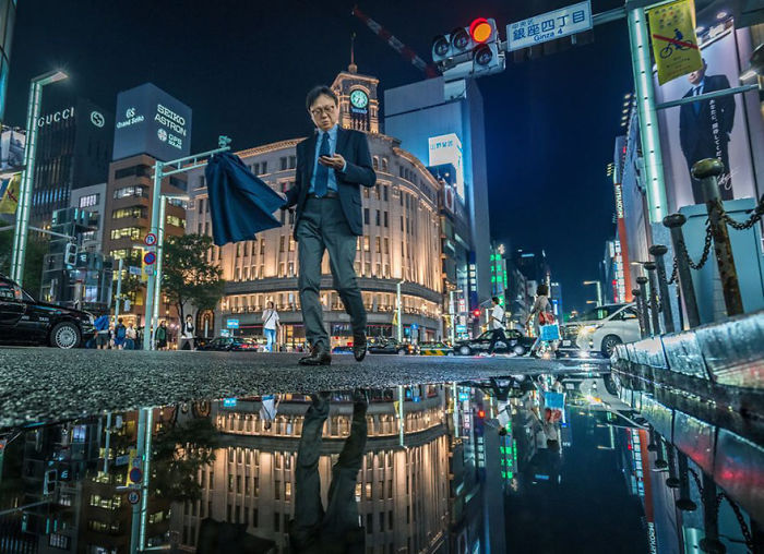 Man walking on rainy Tokyo street at night with reflections in puddles, showcasing Japan street photography urban scenes.