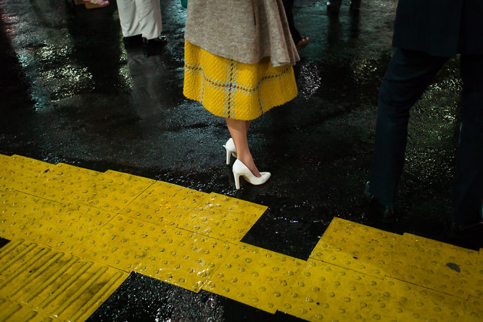 Woman wearing white high heels and a yellow skirt standing on a wet street in Japan street photography scene.