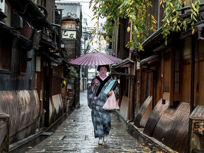 Woman in traditional kimono holding umbrella walking through a narrow street in Japan street photography scene.