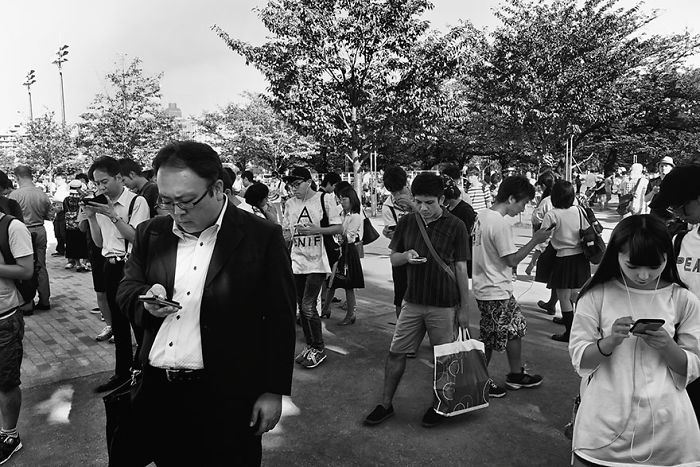 Black and white Japan street photography showing diverse people in a park absorbed in their smartphones and daily activities.
