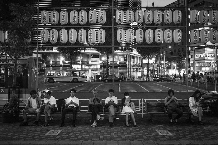 Black and white Japan street photography showing people sitting under traditional lanterns in an urban night setting.
