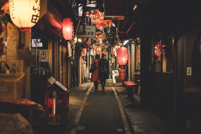 Narrow Japanese street at night with red lanterns and couple walking, showcasing Japan street photography shots.