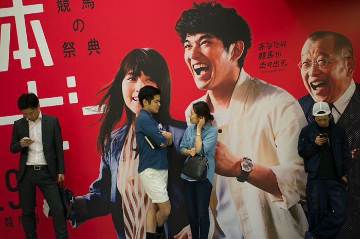 People standing and interacting in front of a vibrant red wall featuring Japan street photography portraits.