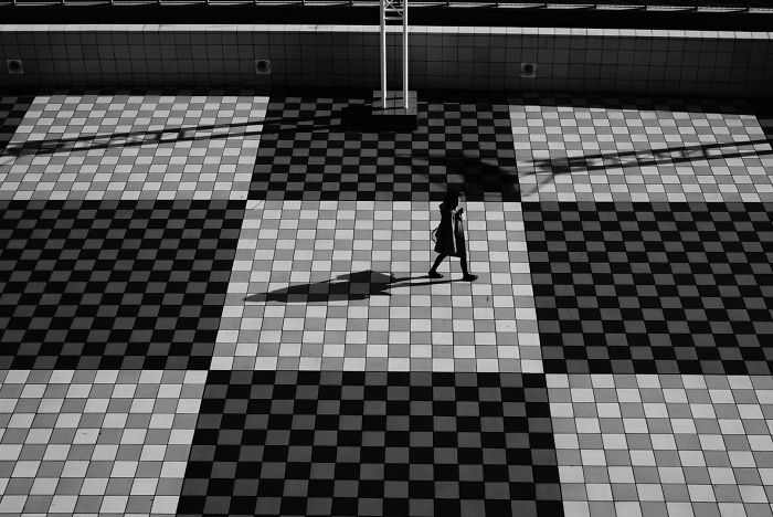 Person walking alone on a checkered tiled street with strong shadows in Japan street photography scene