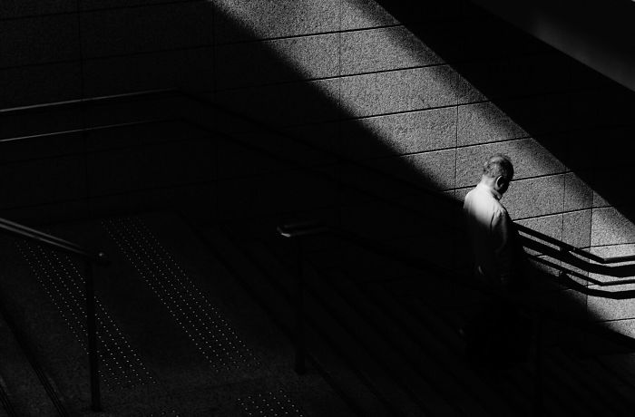 Black and white Japan street photography of a man walking down stairs with dramatic light and shadow contrast.