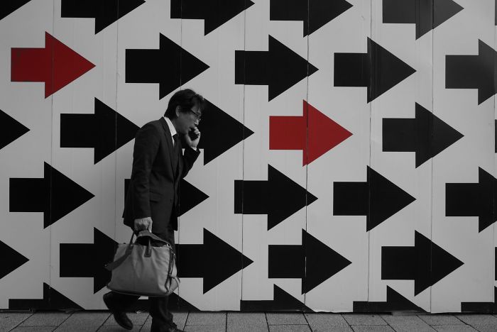 Man in a suit walking and talking on phone against a wall with red and black arrows in Japan street photography shot