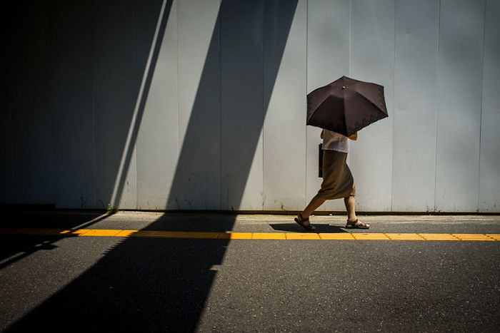 Person walking with an umbrella along a sunlit street in Japan, showcasing rare Japan street photography moments.