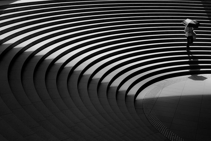 Person with umbrella walking on curved steps in a black and white Japan street photography shot capturing urban patterns.
