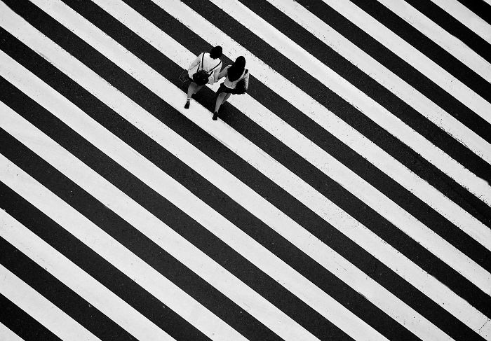 Two people walking across a large black and white striped crosswalk in Japan street photography capturing unique urban scenes.