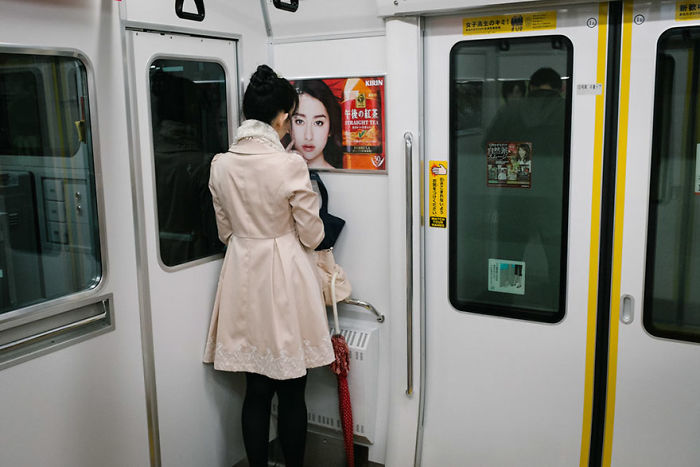 Woman in beige coat standing inside a Japanese train, a candid Japan street photography shot capturing urban daily life.