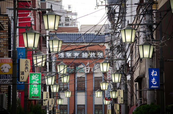Japanese street photography showing a narrow urban alley with hanging lanterns and dense overhead power lines.