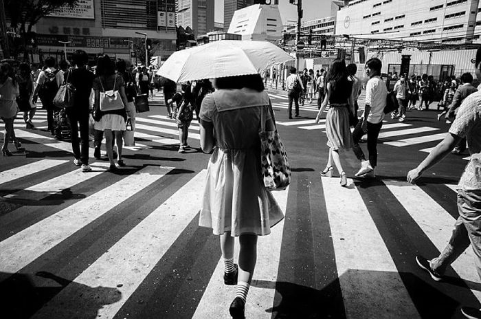 Black and white Japan street photography showing a crowded pedestrian crossing with a woman holding a white umbrella.