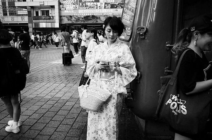 Black and white Japan street photography showing a woman in traditional attire using her phone on a busy city sidewalk.