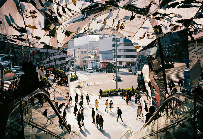 Reflection-filled urban scene in Japan with people walking near a busy street, showcasing Japan street photography elements.