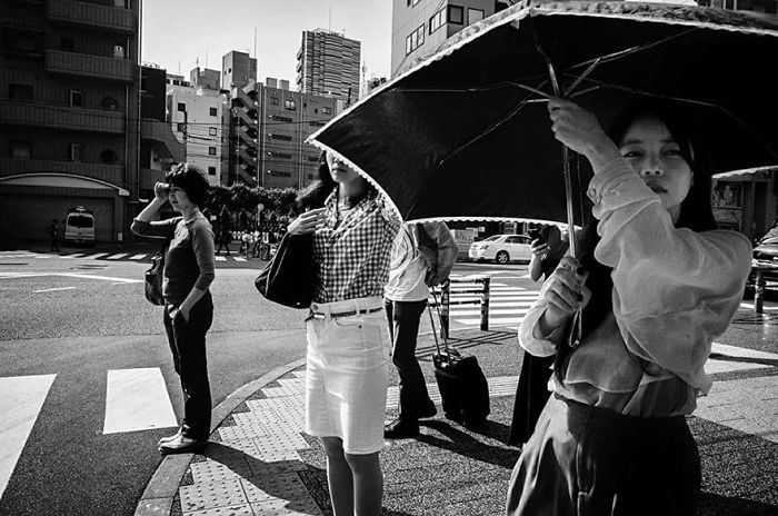 Black and white Japan street photography of people waiting on a city crosswalk with urban buildings in the background.