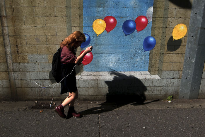 Young woman walking past colorful balloon wall art in urban street scene, a striking example of Japan street photography shots.