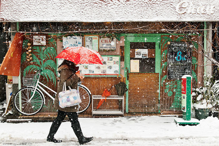 Person walking with red umbrella in snowy Japan street scene, showcasing unique Japan street photography capturing rare urban moments.