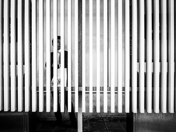 Black and white Japan street photography showing a man standing behind vertical panels in an urban setting.
