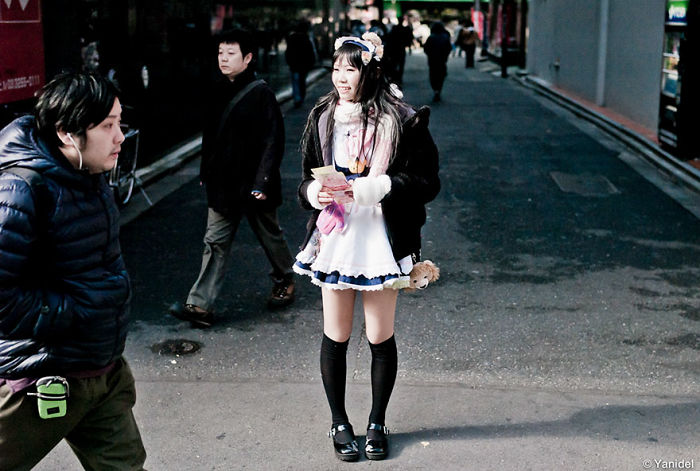 Young woman in cosplay outfit smiling on a street with pedestrians, showcasing Japan street photography with rare urban moments.