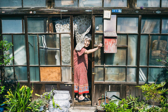 Elderly woman opening door of a traditional wooden house in Japan street photography capturing daily life moments.