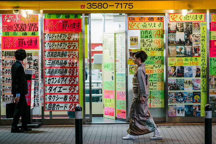 Man in suit and woman in traditional kimono walking past a colorful storefront in Japan street photography.
