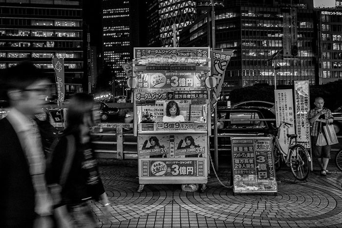 Black and white Japan street photography showing a busy urban scene with blurred pedestrians and illuminated buildings at night.