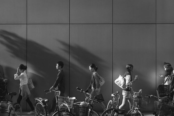 Black and white Japan street photography showing people walking with bicycles against a tiled wall in urban setting.