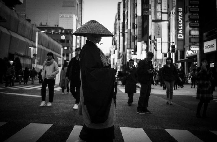 Black and white Japan street photography showing a person in traditional attire crossing a busy urban intersection.