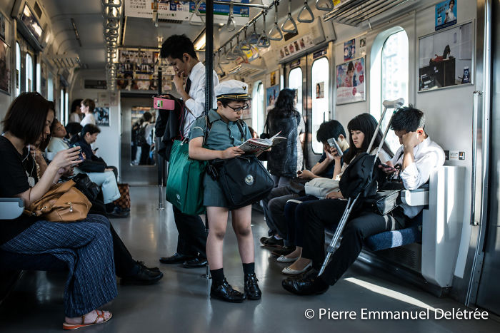 Young boy reading a book on a crowded train, surrounded by passengers using phones in Japan street photography shot